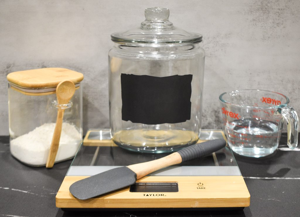 Jar with flour, water, and scale on a counter
