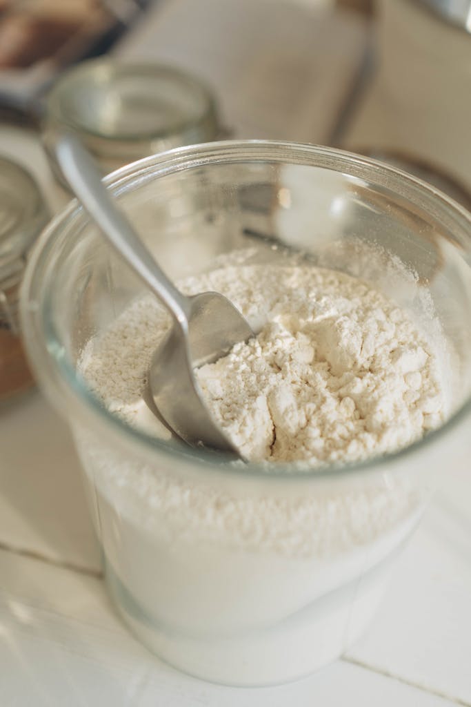 A close-up of a glass jar filled with flour and a metal spoon, ideal for baking themes.