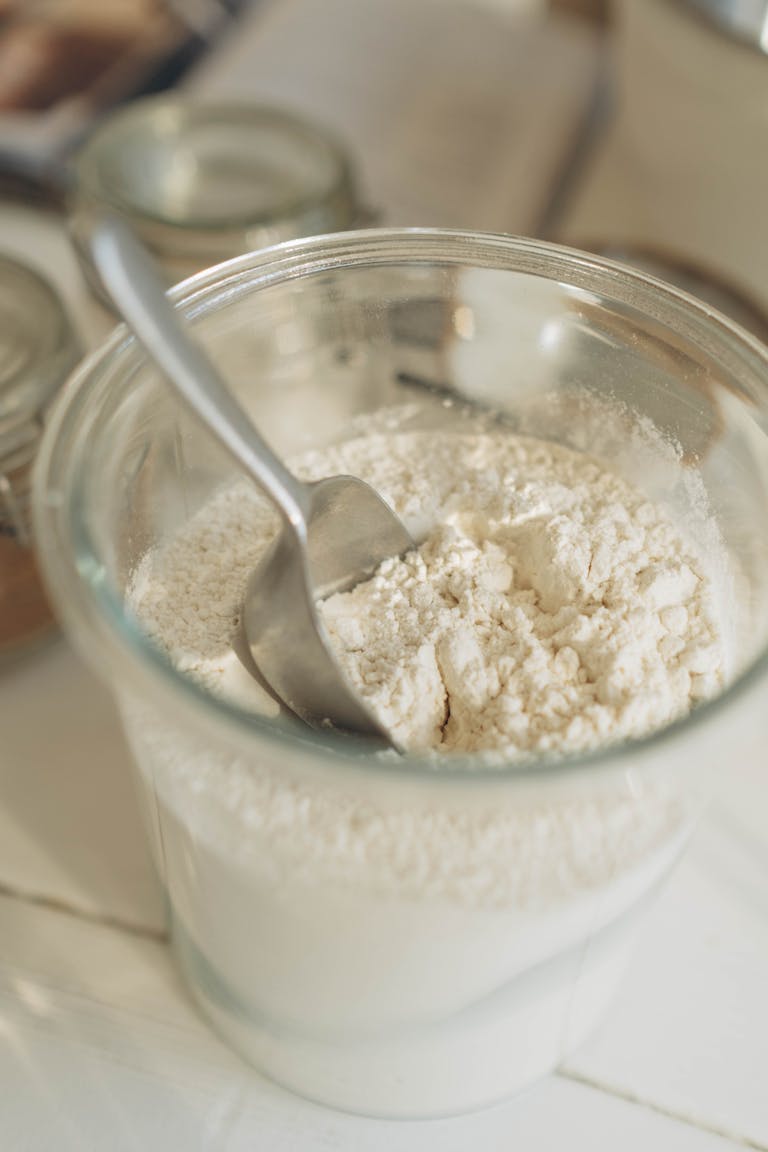 A close-up of a glass jar filled with flour and a metal spoon, ideal for baking themes.