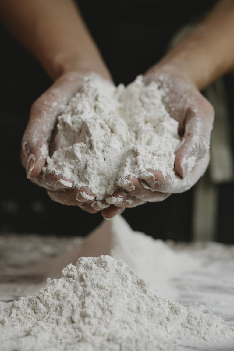 Close-up of a person holding a mound of organic flour in their hands inside a kitchen.