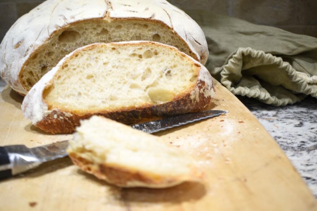 a loaf of bread and a knife on a cutting board and a linen bag to show how long does sourdough bread last
