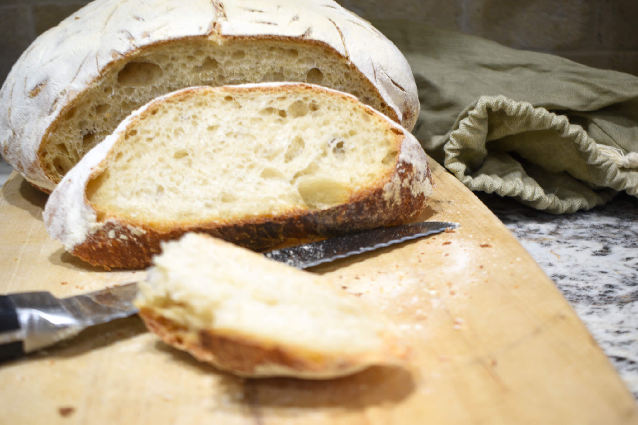 a loaf of bread and a knife on a cutting board and a linen bag to show how long does sourdough bread last